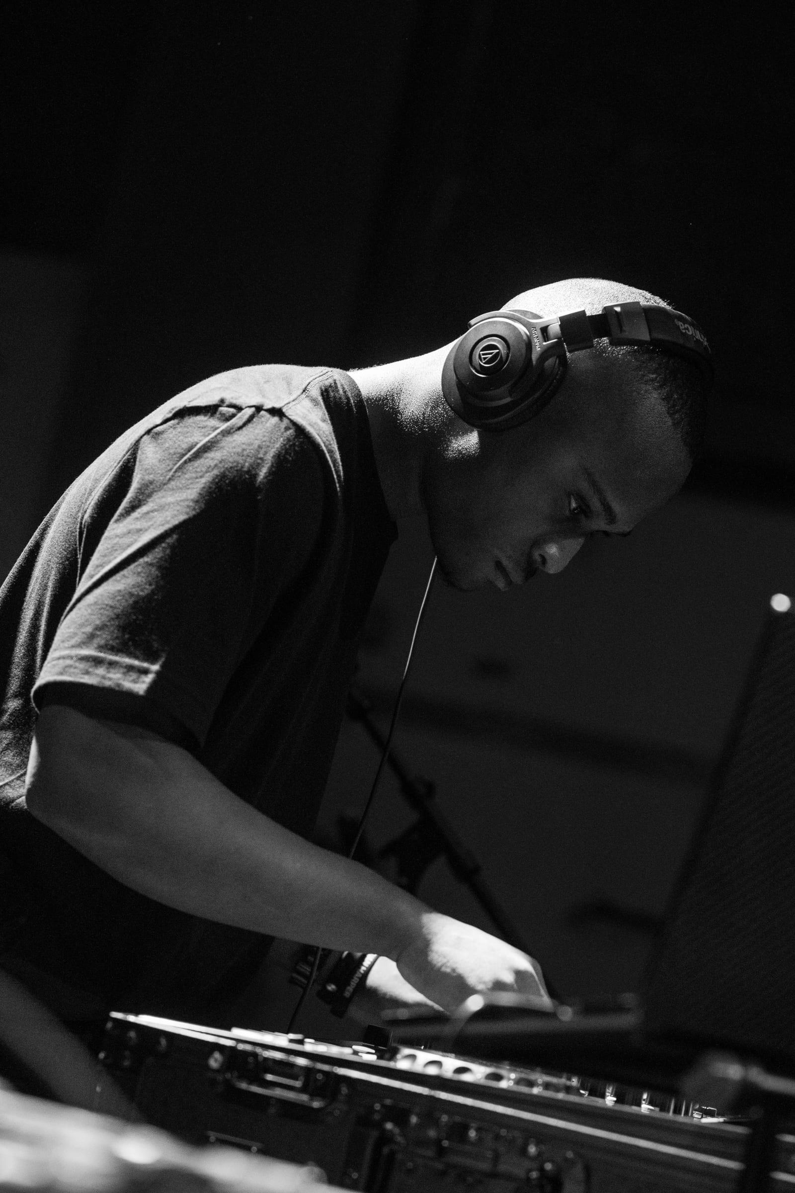 Black-and-white profile of MH with head down and hands on the decks