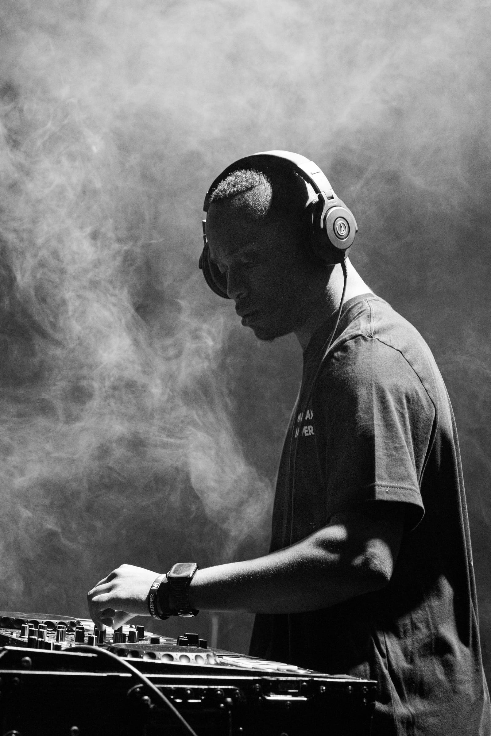 Black-and-white frame of MH in headphones, surrounded by stage haze