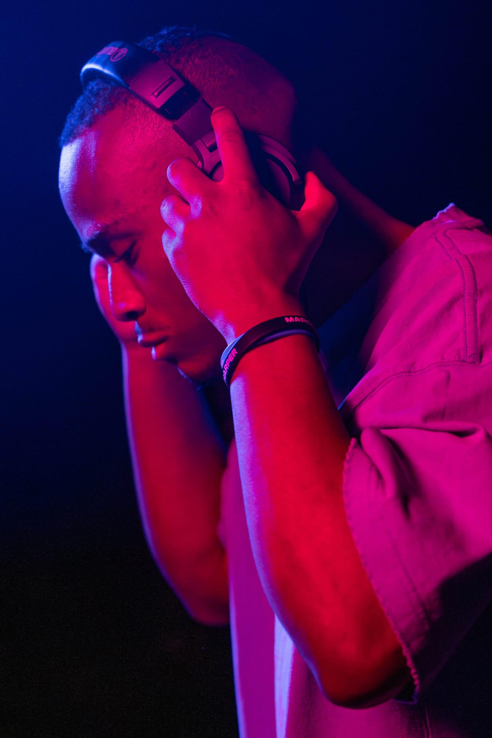 Close portrait of MH with both hands on his headphones, lit in magenta and blue